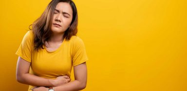 A woman in a yellow t-shirt holding her stomach, as if in pain.