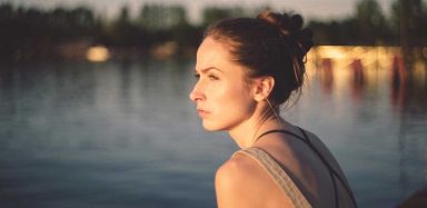 A picture of a women in front of a body of water staring off into space