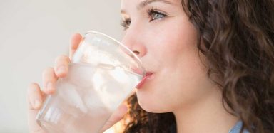 A side view headshot of a Caucasian woman with brown hair drinking a glass of water.