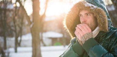 A person wearing a coat outside in the winter, trying to warm their hands up.