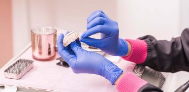 A dentist wearing blue latex gloves holding fake teeth.