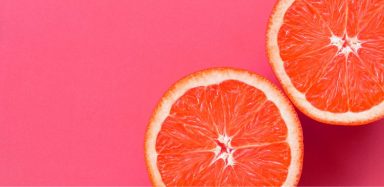 A pink grapefruit cut in half, sitting against a light pink background.