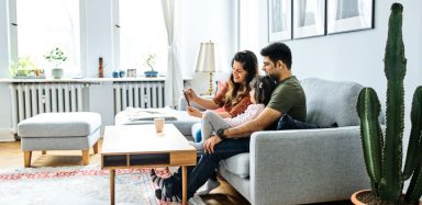 A family sitting together on a grey couch in they living room.